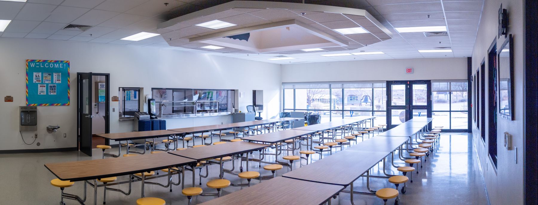 Brightly lit school cafeteria featuring tables and chairs arranged for students to sit and eat together.