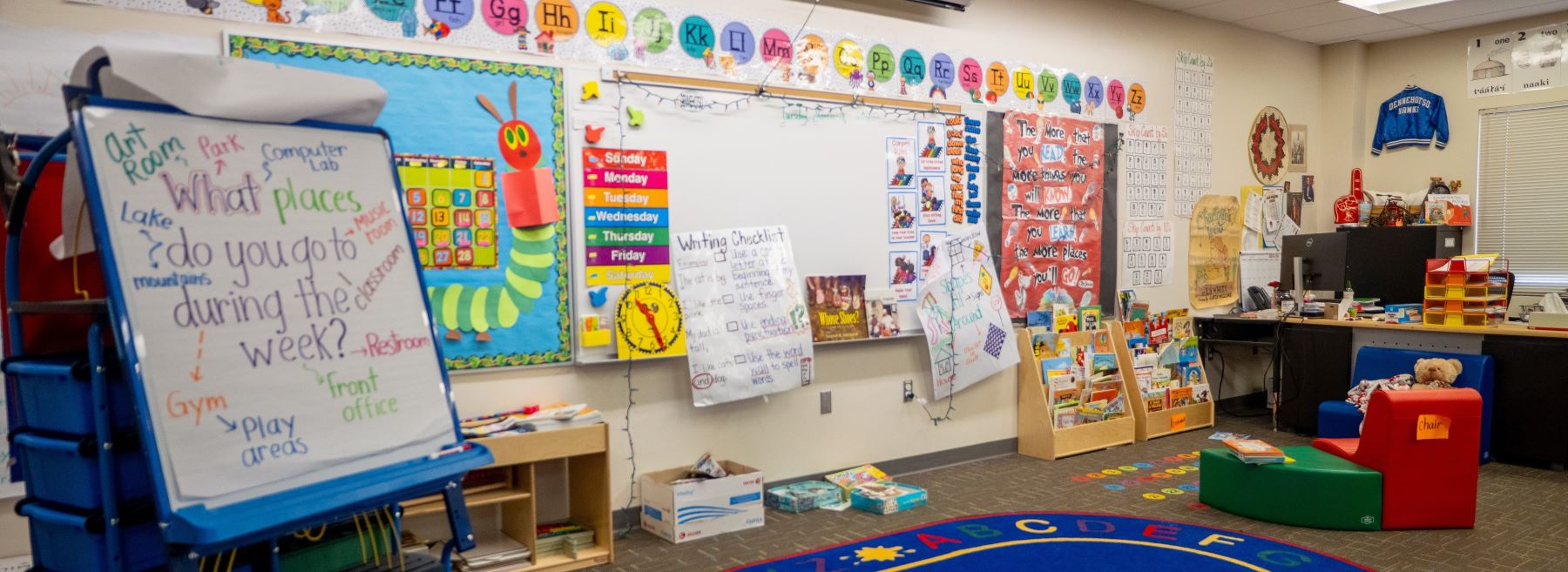 Inside a bright and colorful school classroom, a large whiteboard and chalkboard are prominently displayed at the front, ready for lessons.